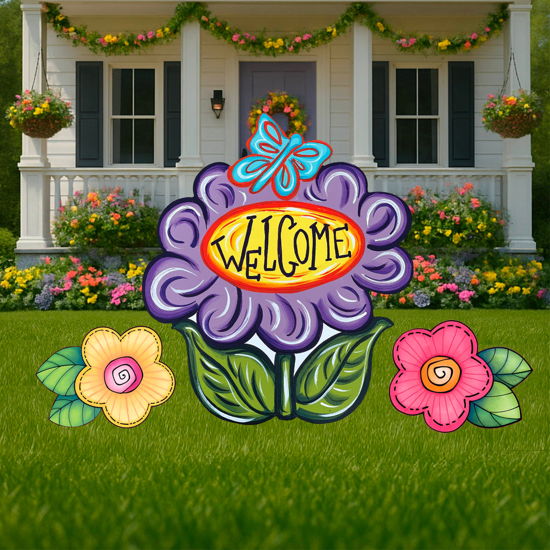 Spring and Summer Outdoor Yard Flower Signs and Decor featuring three flowers - pink, yellow and purple.  Purple flower lawn sign has the word welcome in it. Personalize flower yard decorations at Yard Art Decor and More