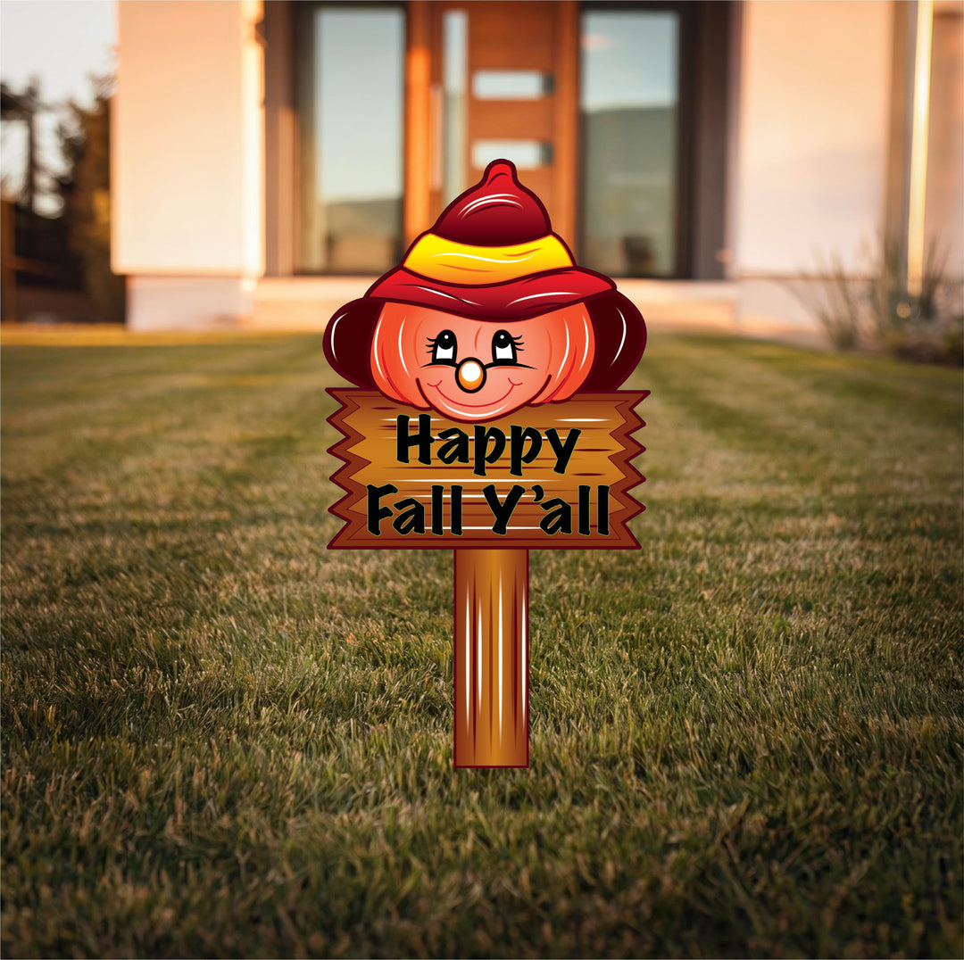 Happy Fall Y’all metal yard sign featuring a smiling pumpkin in a red and yellow hat, displayed on a green lawn in front of a modern home