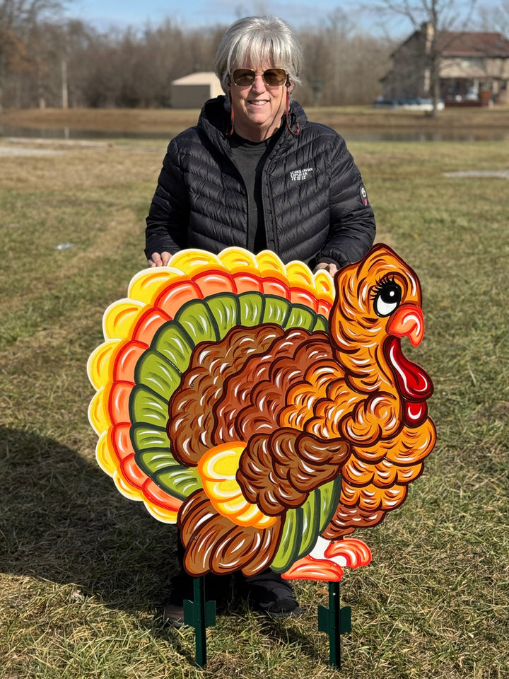 Person holding a large, colorful turkey decorative sign outdoors.
