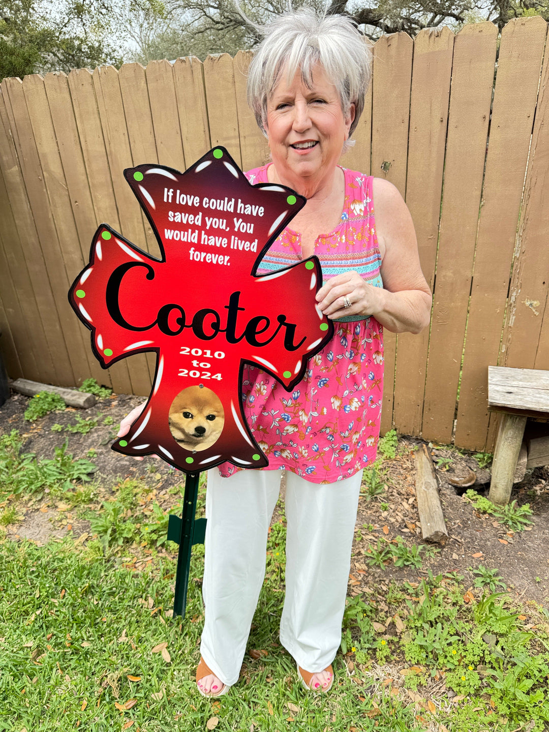 Mary, the owner of Yard Art Decor and More holding a red pet memorial yard cross. This customizable memorial cross can include your pets name, date of birth, a favorite quote and more. 