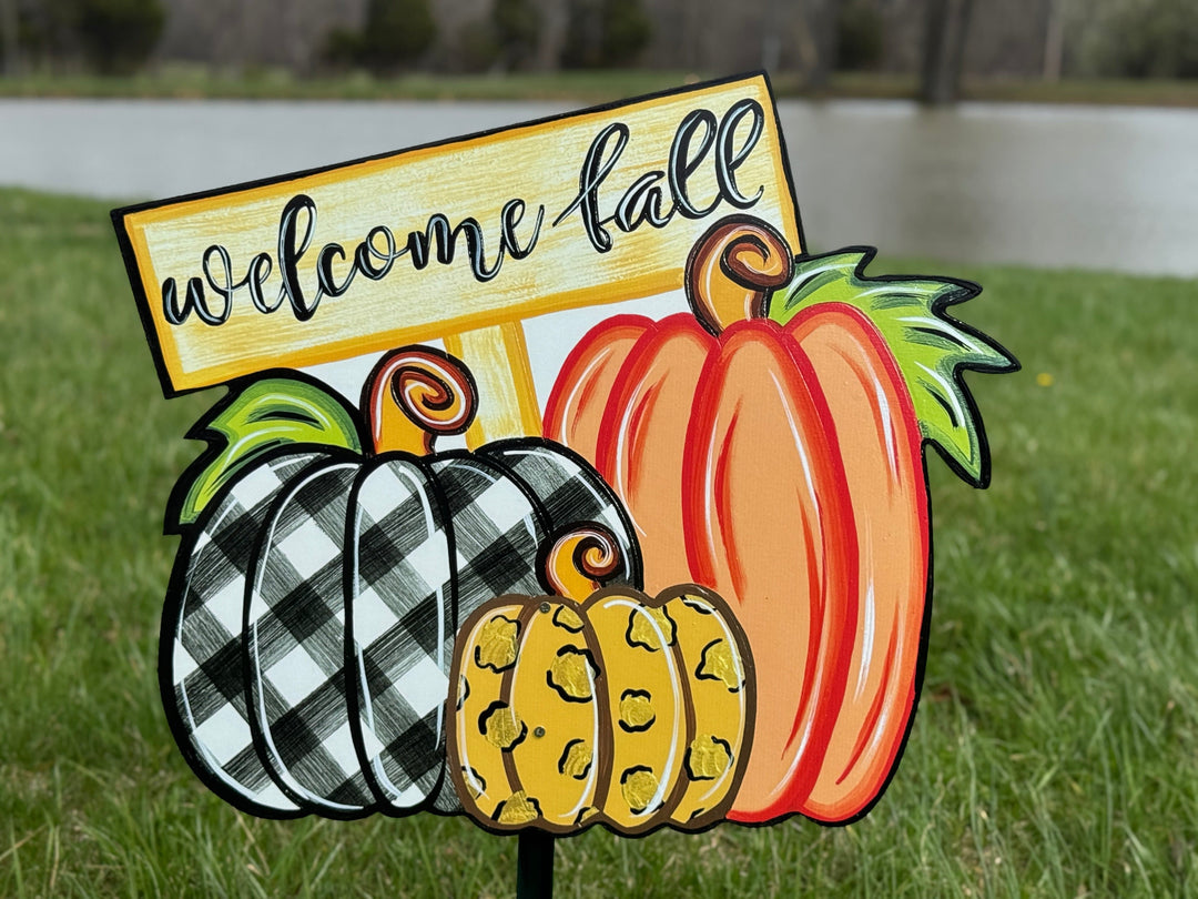Welcome Fall Sign on top of three Fall pumpkins yard art decoration: one pumpkin is black and white plaid, one pumpkin is leopard print, and one pumpkin is orange