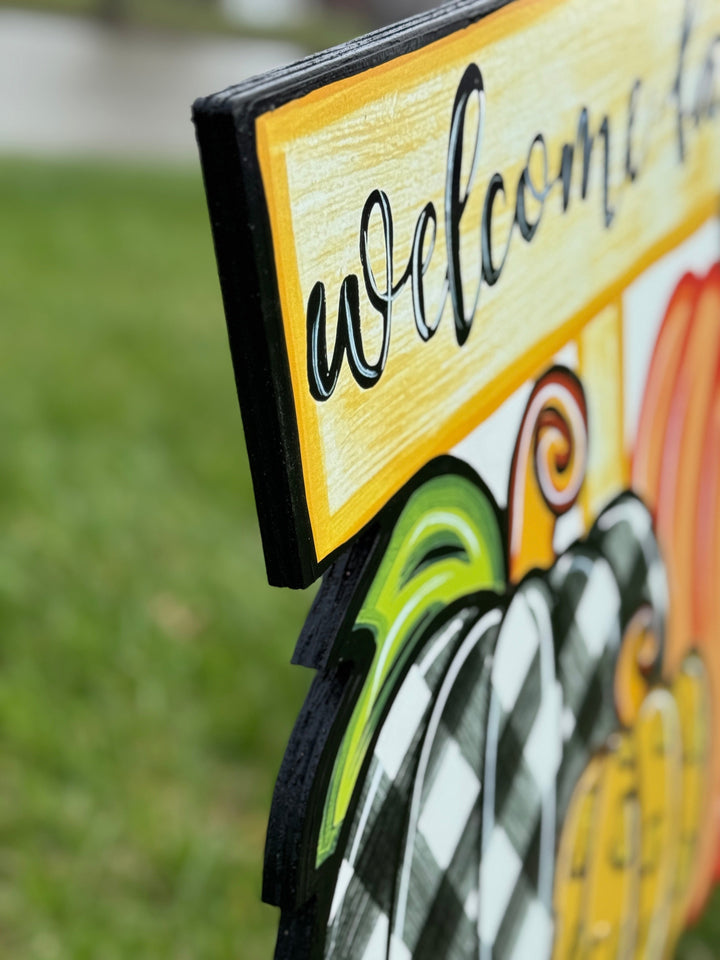 side view of Welcome Fall Sign on top of three Fall pumpkins yard art decoration: one pumpkin is black and white plaid, one pumpkin is leopard print, and one pumpkin is orange