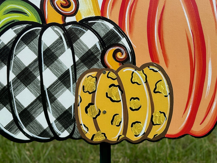 close up view of leopard print pumpkin on Welcome Fall Sign on top of three Fall pumpkins yard art decoration: one pumpkin is black and white plaid, one pumpkin is leopard print, and one pumpkin is orange