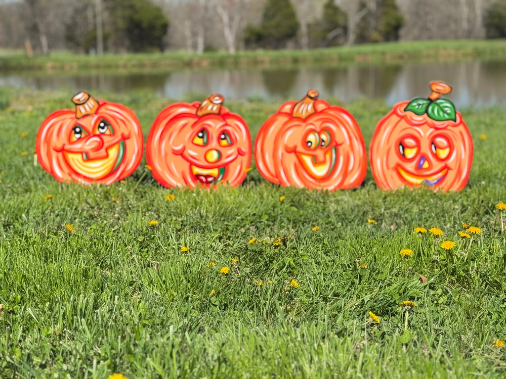 Four Halloween-themed pumpkin decorations on grass with a lake in the background