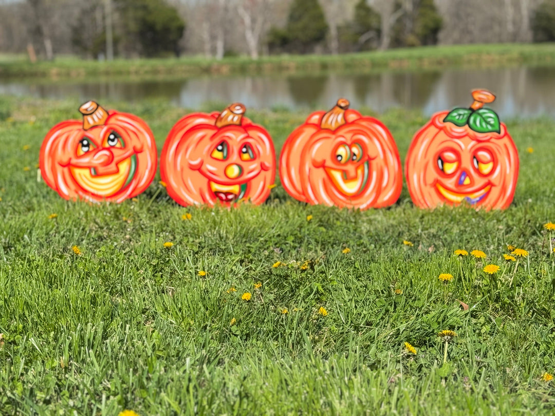 Four Halloween-themed pumpkin decorations on grass with a lake in the background