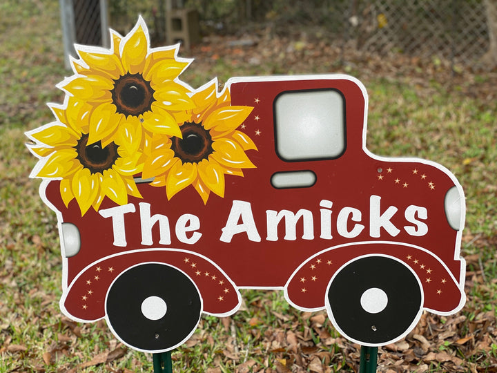 Personalized yard sign of a red truck that has the owners last name on it. In the bed of the pick up truck are 3 yellow sunflowers. Custom yard art signs with stakes available at Yard Art Decor and More. 