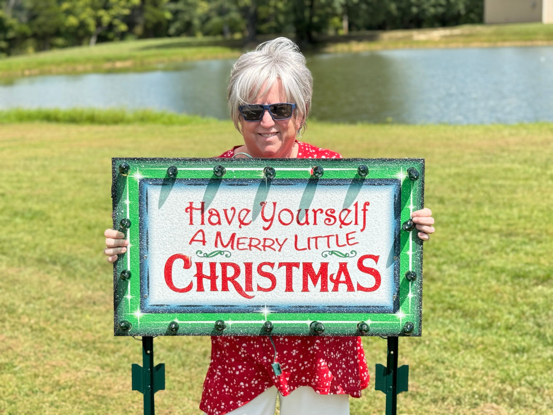 Person holding a Christmas sign with text outdoors