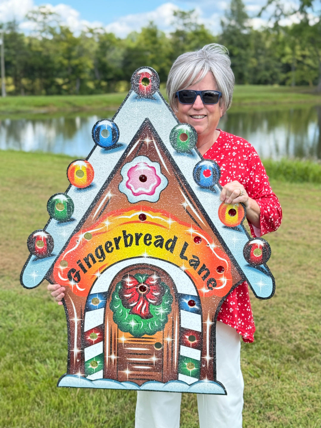 Person holding a colorful gingerbread-themed sign with 'Gingerbread Lane' text outdoors.
