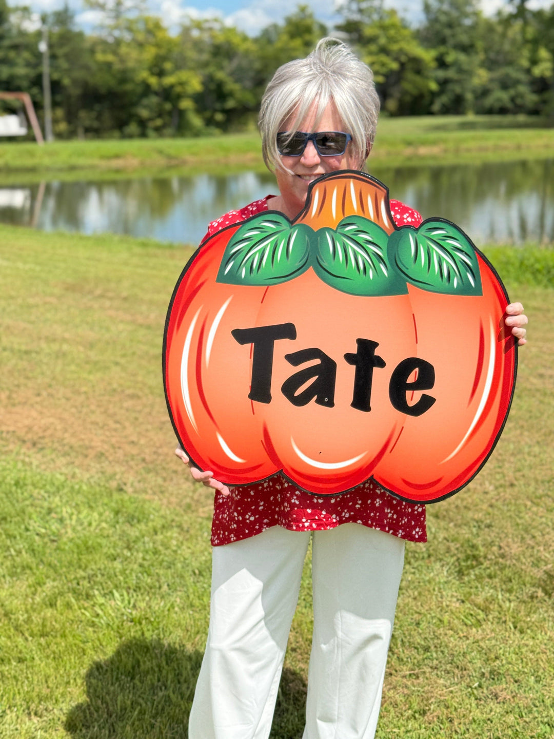 Person holding a pumpkin-shaped sign with 'Tate' on it in an outdoor setting.