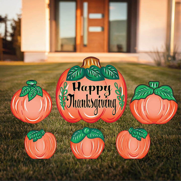 Thanksgiving yard sign display featuring a large pumpkin with the message "Happy Thanksgiving" surrounded by smaller pumpkins, set on a neatly trimmed lawn in front of a modern home.