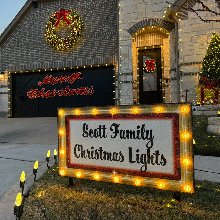 Illuminated custom Christmas yard decorations with warm glowing marquee lights displayed on a front lawn driveway landscape at dusk.