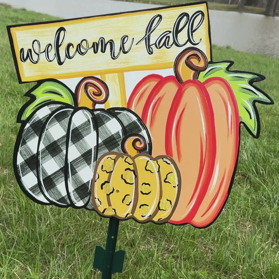 video of Welcome Fall Sign on top of three Fall pumpkins yard art decoration: one pumpkin is black and white plaid, one pumpkin is leopard print, and one pumpkin is orange