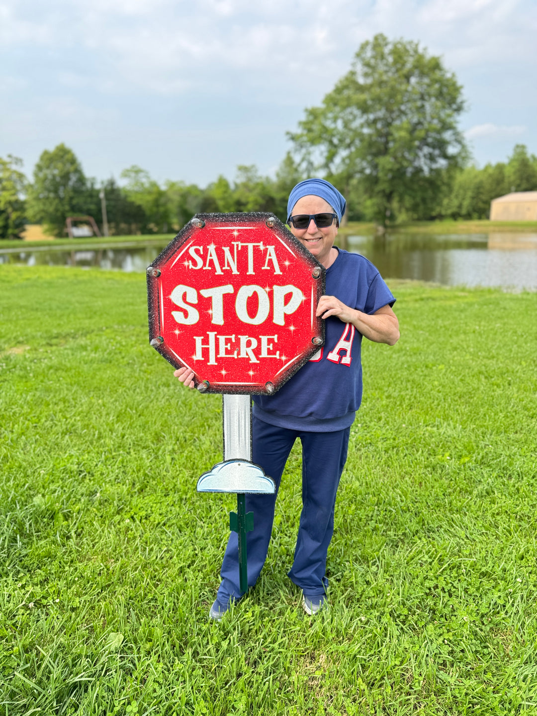 Owner holding large “Santa Stop Here” glitter yard sign outdoors – size reference for holiday lawn display.