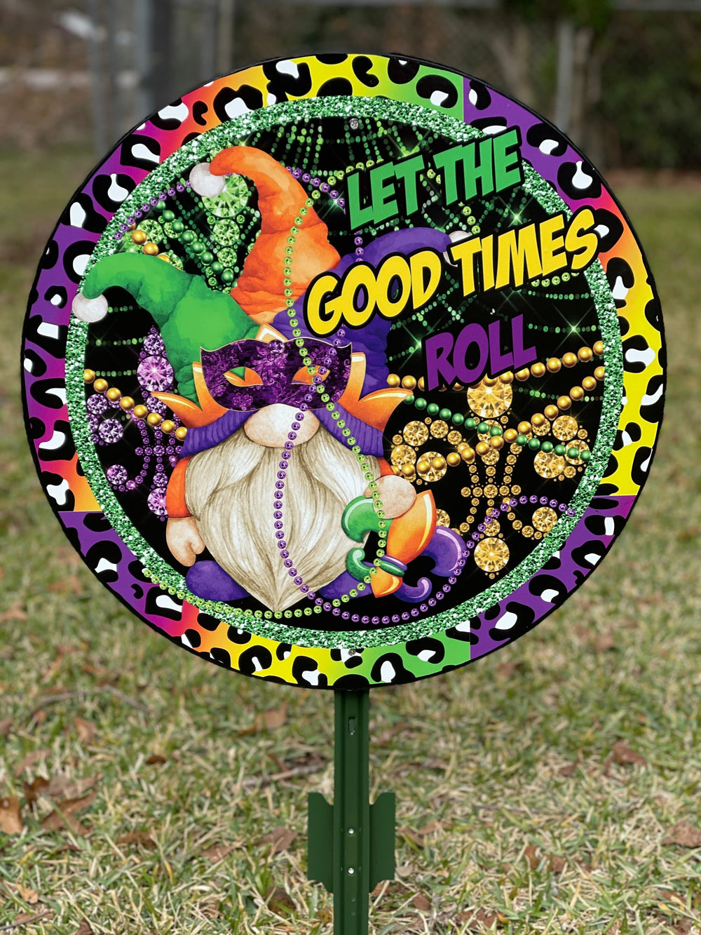 Garden gnome dressed in Mardi Gras clothing and beads in a Mardi Gras themed sign that reads, "Let the Good Times Roll." Traditional Mardi Gras colors. Yard and lawn decorations for the Holidays available for sale at Yard Art Decor and More. 