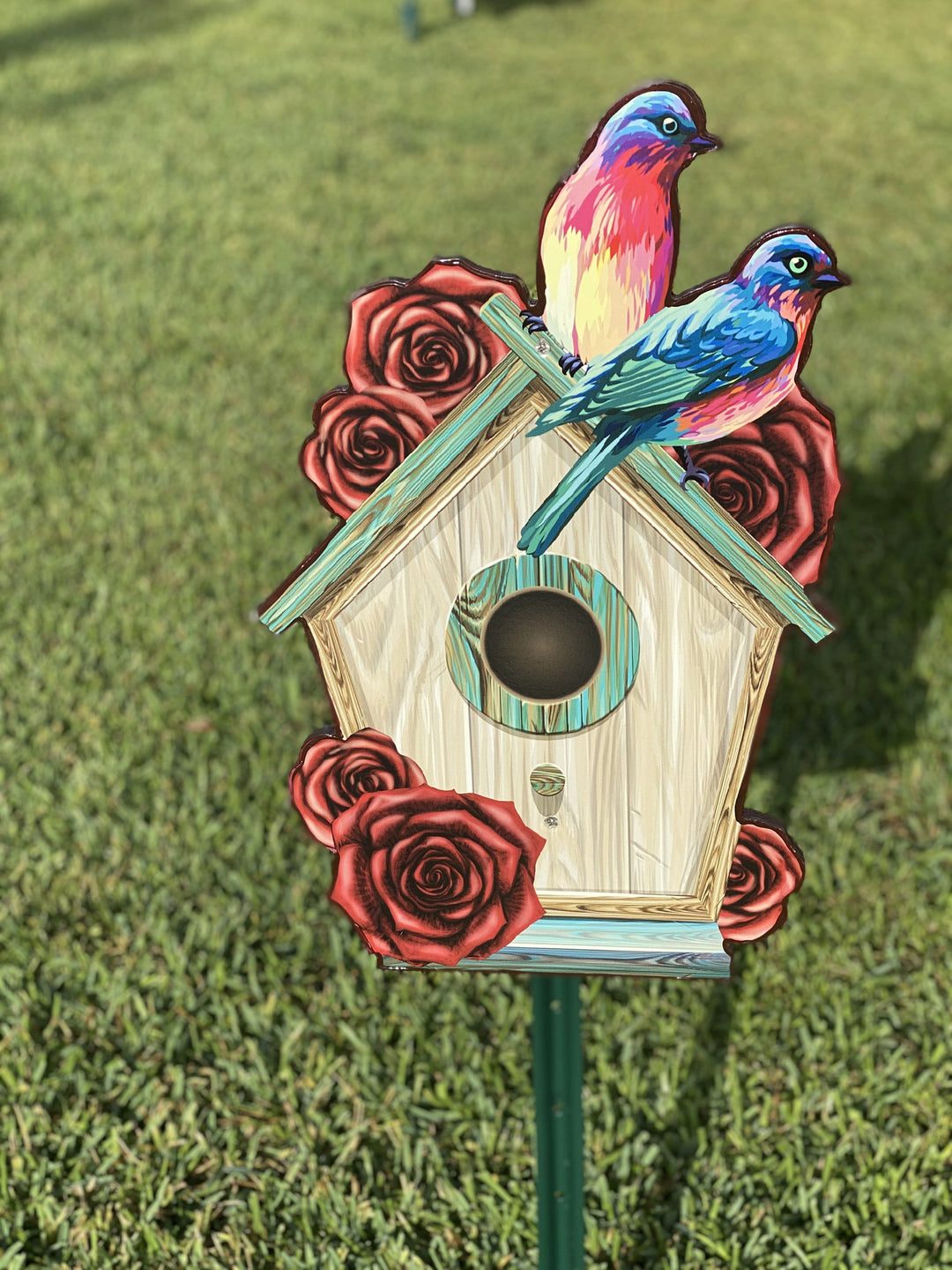 Outdoor Yard Decor - Birdhouse yard sign in tan with green roof featuring 2 birds in blue, yellow and red on top of the birdhouse. Also decorated with red roses. Hand Painted bird yard and lawn decorations for sale. 